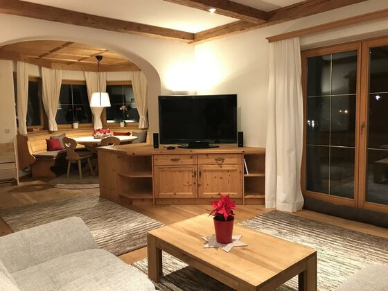 Wohnzimmer mit Holzmöbeln, Fernseher, Couch und angrenzender Essecke in einer Ferienwohnung.