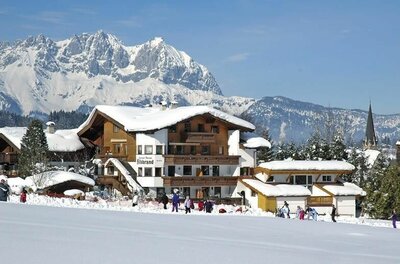 Appartmentpension Hillebrand im Winter Schneebedeckte Appartmentpension Hillebrand vor einem massiven, felsigen Gebirgspanorama im Winter.