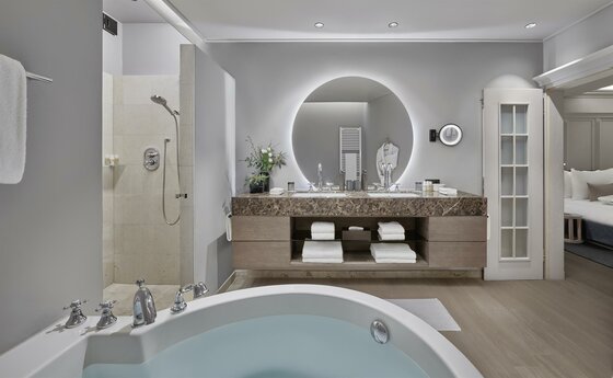 Badezimmer Deluxe Suite Residenz Modernes Badezimmer mit runder Badewanne, Doppelwaschtisch, beleuchtetem Rundspiegel und Dusche.