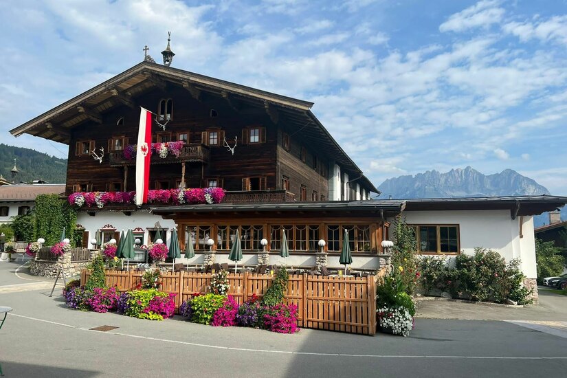Traditionelles Holzgebäude mit Blumenschmuck, Außenterrasse und Bergpanorama im Hintergrund.