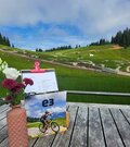 Holztisch mit Blumen und Speisekarte vor einem Bikepark im Hintergrund.