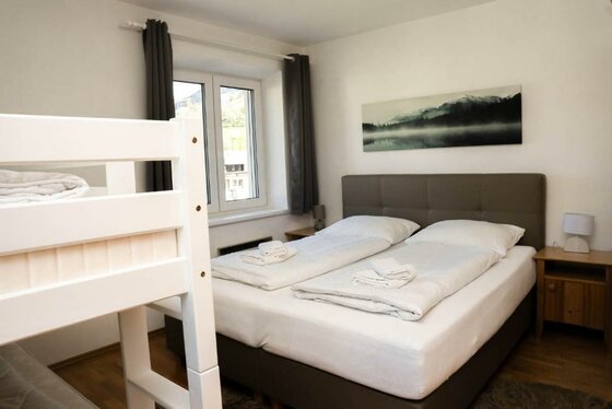 587402270 Ein gemütliches Schlafzimmer mit einem Doppelbett und einem Etagenbett. Große Fenster sorgen für viel Tageslicht.