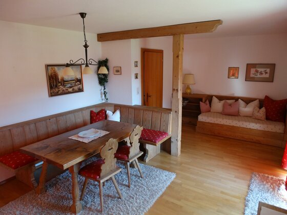 Wohnbereich Sommerau Rustikaler Wohnraum mit Holzesstisch, Eckbank und einem Sofa mit rot-weißen Kissen.