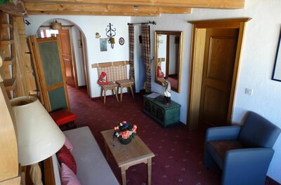 Wohnraum 1 im Haus Wörgötter Rustikaler Wohnraum mit Holzbalkendecke, Sofa, Sessel und rotem Teppichboden.