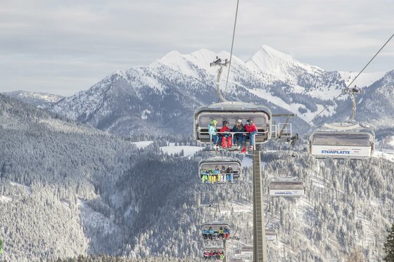 Eine Skiliftfahrt in den Bergen mit schneebedeckten Gipfeln im Hintergrund. Die Landschaft ist winterlich und idyllisch.