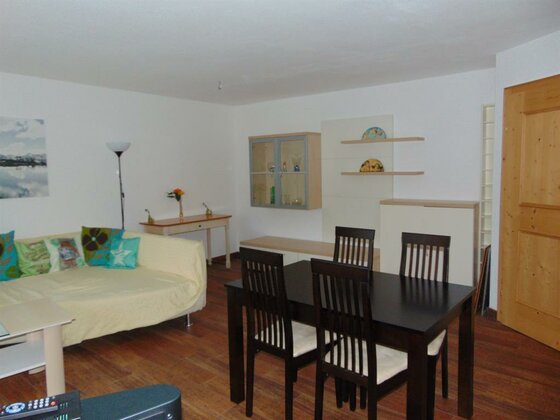 Apartment 2 Essbereich Wohn- und Essbereich mit dunklem Holztisch, vier Stühlen und hellem Sofa vor weißer Wand.