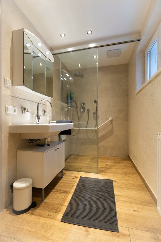 immbolie -5 Ein modernes Badezimmer mit einer Glasdusche und einem Doppelwaschbecken. Der Boden ist aus Holz und es gibt ein großes Fenster.
