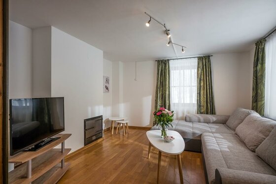 Wohnzimmer Haus Wetti Wohnzimmer mit grauem Ecksofa, weißem Couchtisch, Fernseher und Kaminofen auf Parkettboden.