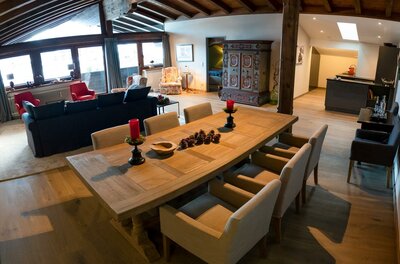 Moderner Wohn- und Essbereich mit großem Holztisch, dunklem Sofa und rustikalem Schrank unter einer Dachschräge.