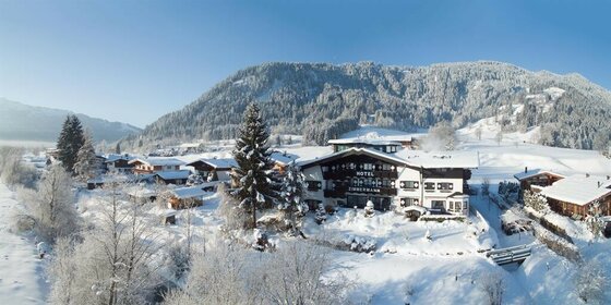 Verschneites Hotel Zimmermann in einer alpinen Winterlandschaft mit bewaldeten Bergen im Hintergrund.