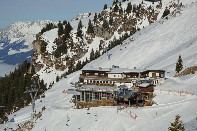 Blick auf das Alpenhaus am Kitzbüheler Horn mit Seilbahnanlagen und verschneiten Skipisten.