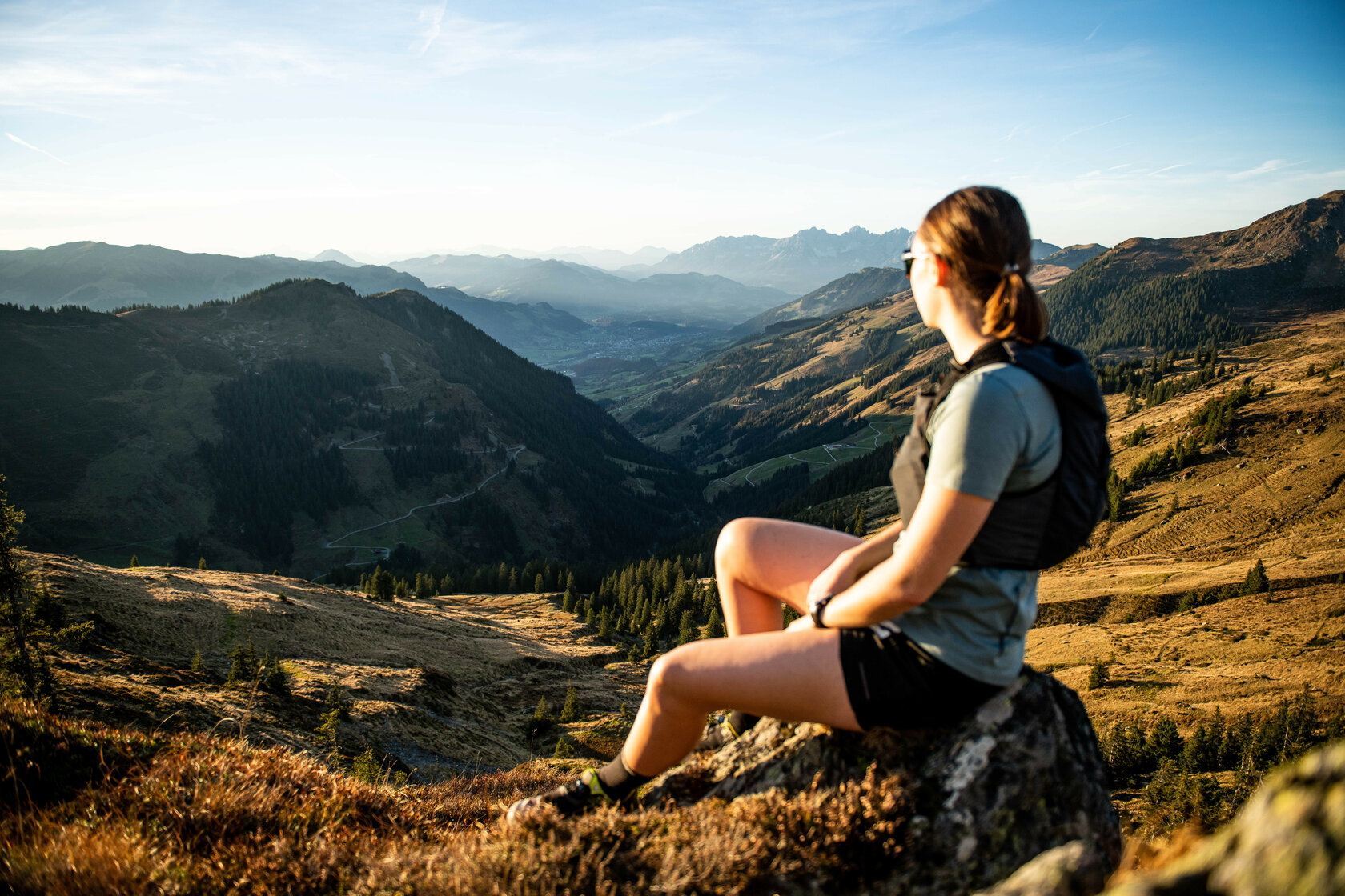Umgeben von sanften Hügeln und Wäldern, sitzt die Frau auf einem Felsen und betrachtet die weite Aussicht auf das Tal.