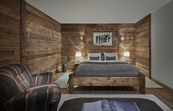 Doppelbett aus Holz in einem Zimmer mit Holzwänden, Nachttischlampen und einem gemusterten Sessel.