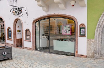 Schaufenster eines Optikergeschäfts mit Rundbogen in einer gepflasterten Fußgängerzone.