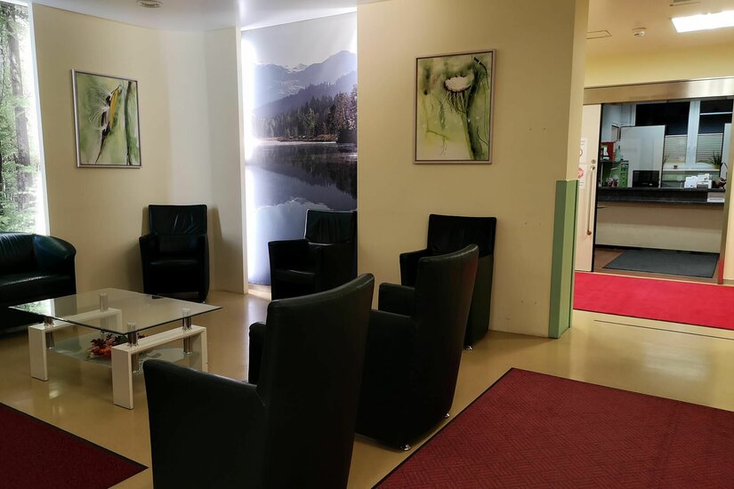 Wartebereich mit schwarzen Ledersesseln, Glastisch und Landschaftsbildern an den Wänden.