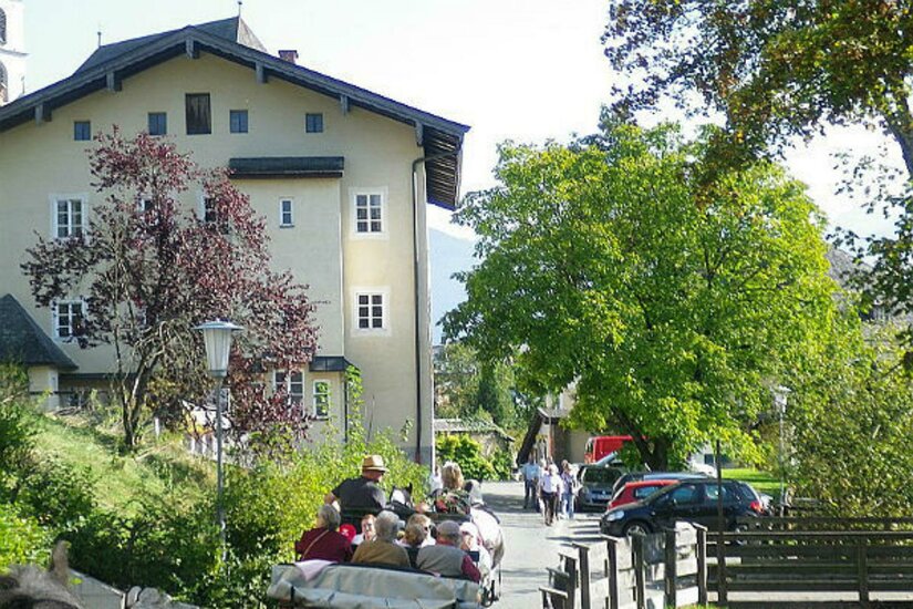 Eine ruhige Straße mit einem großen Gebäude im Hintergrund. Menschen sitzen in einem offenen Fahrzeug und genießen die Landschaft.