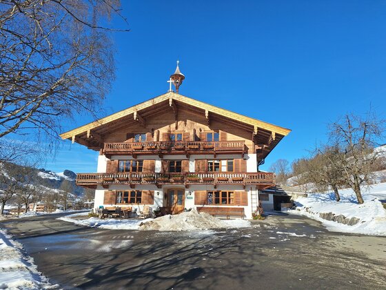 Ein traditionelles Chalet in den Alpen mit einem Holzfassade. Es ist schneebedeckt und es scheint ein klarer blauer Himmel zu sein.
