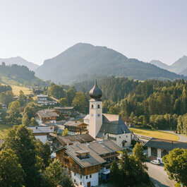 Eine malerische Berglandschaft mit einem charmanten Dorf, das von sanften Hügeln und hohen Bergen umgeben ist.