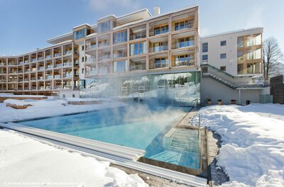 Dampfender Außenpool eines modernen Hotelgebäudes in einer verschneiten Winterlandschaft.