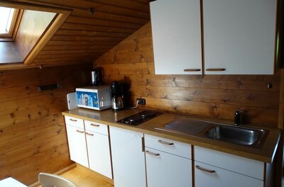 Kleine Küchenzeile mit weißen Fronten unter einer Holzschräge mit Dachfenster.