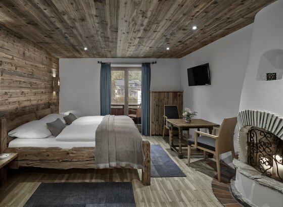 Rustikales Hotelzimmer mit Doppelbett aus Altholz, Sitzecke und offenem Kamin.
