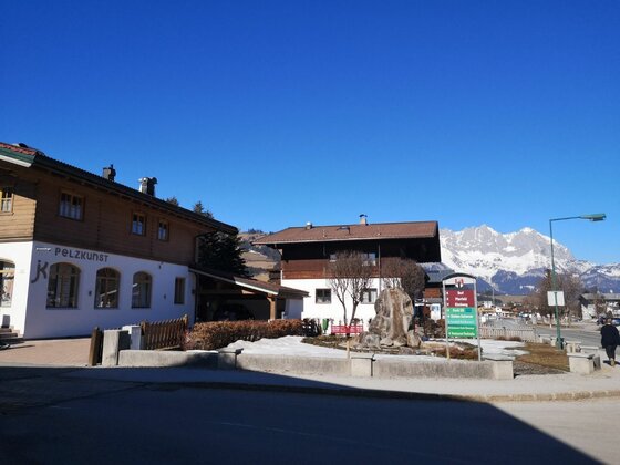 Ortsansicht mit Bergpanorama Alpiner Ort mit traditionellen Holzhäusern vor schneebedeckten Bergen unter blauem Himmel.