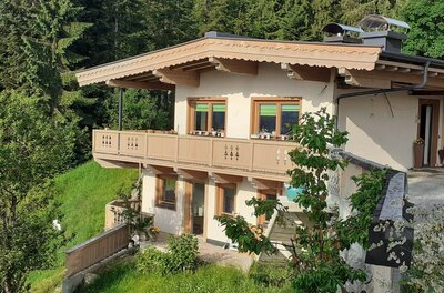 Ferienwohnung Waldglück Zweistöckiges Gebäude mit Holzfassade und Balkon vor einem Nadelwald.