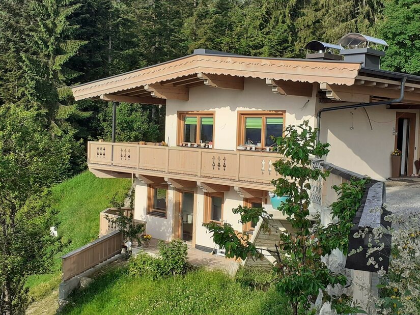 Zweistöckiges Gebäude mit Holzfassade und Balkon vor einem Nadelwald.