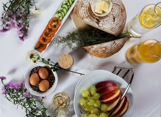 Frühstückstisch mit Brot, Butter, Eiern, Obst, Gemüse und Säften aus der Vogelperspektive.
