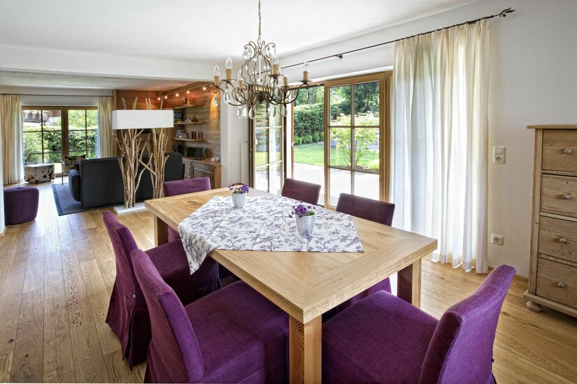 Holztisch mit lila Stühlen in einem hellen Wohn- und Essbereich mit Parkettboden.