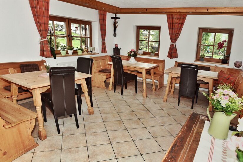 Rustikaler Gastraum mit Holztischen, Eckbänken und dunklen Lederstühlen auf Fliesenboden.