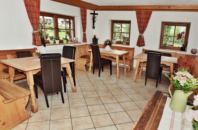 Rustikaler Gastraum mit Holztischen, Eckbänken und dunklen Lederstühlen auf Fliesenboden.