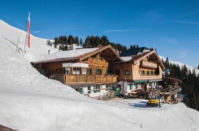 Alpiner Berggasthof aus Holz in einer verschneiten Winterlandschaft unter blauem Himmel.
