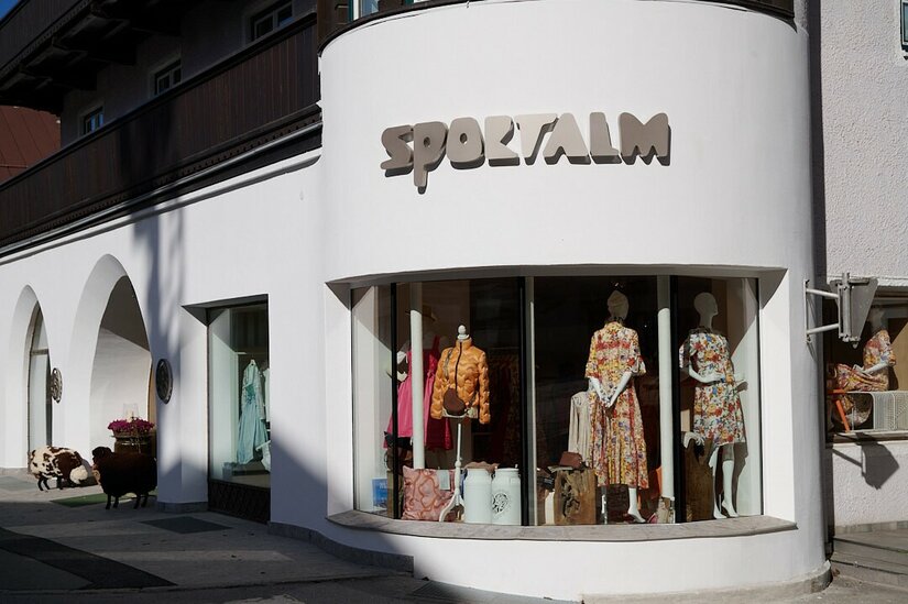 Außenansicht eines Bekleidungsgeschäfts mit Schaufenstern und dem Schriftzug Sportalm an einer weißen Fassade.