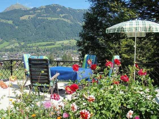 Sonnenterrasse mit Gartenmöbeln, Blumenbeeten und Blick auf bewaldete Berge und ein Tal.