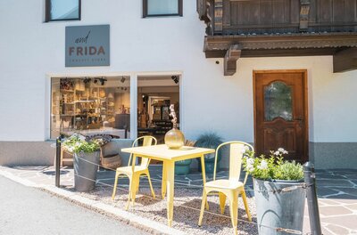 Außenansicht des Concept Stores undFRIDA mit gelben Metallstühlen und einem Tisch vor dem Schaufenster.