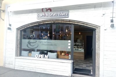 Außenansicht einer italienischen Eisdiele mit weißer Holzfassade und großem Schaufenster.