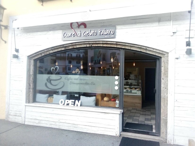 Außenansicht einer italienischen Eisdiele mit weißer Holzfassade und großem Schaufenster.