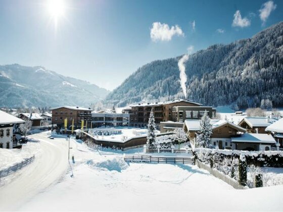 Kitzbühel Lodge im Winter Verschneite Hotelanlage Kitzbühel Lodge vor bewaldeten Bergen bei Sonnenschein.