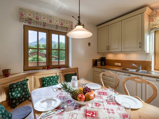 Rustikale Küche mit Esstisch, Eckbank und Blick durch das Fenster auf die Berge.