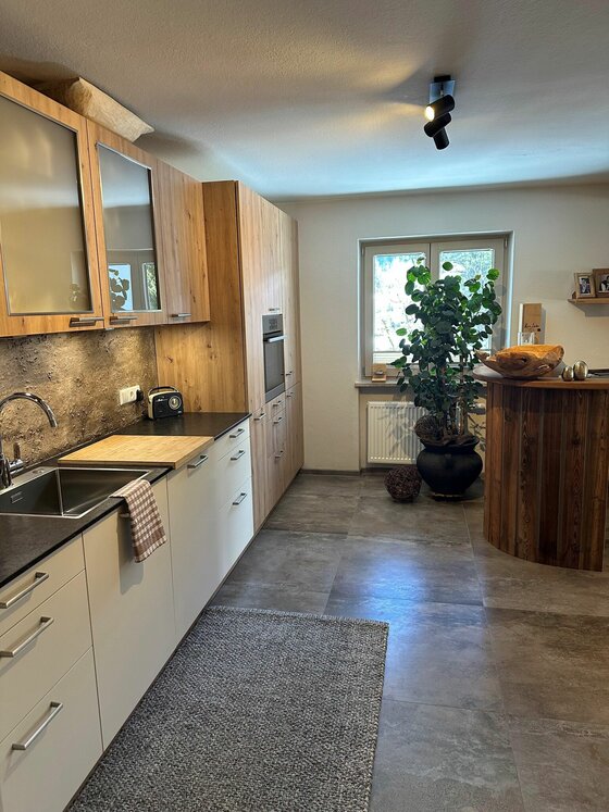 Moderne Einbauküche mit Holzfronten, dunkler Arbeitsplatte und einem runden Holztresen.