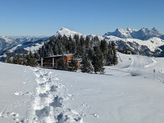 Schneeschuhwandern im Hochgebirge Schneeschuhspur im tiefen Schnee führt zu einer Holzhütte vor verschneitem Bergpanorama.