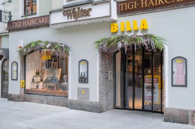 Eingangsbereich eines Billa Supermarktes in einem historischen Gebäude mit Blumendekoration über Tür und Schaufenster.