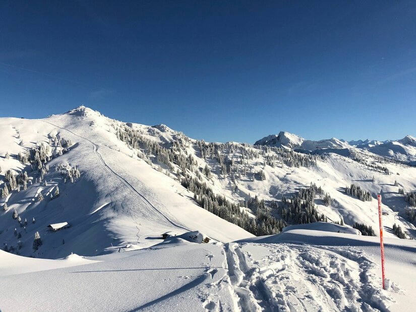 Verschneite Berglandschaft mit Skispuren im Vordergrund und Blick auf den Hochetzkogel unter blauem Himmel.