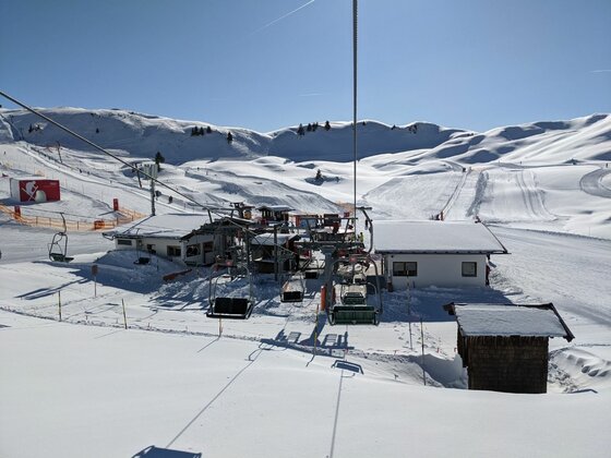 Sessellift und Skistation im Winter Blick aus einem Sessellift auf eine Talstation in einem verschneiten Skigebiet unter blauem Himmel.