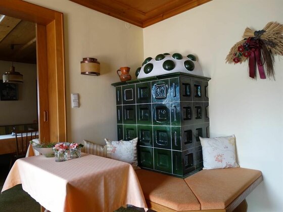 Frühstücksraum im Gästehaus Wallner Rustikaler Kachelofen in Dunkelgrün neben einer Sitzecke mit gedecktem Tisch.