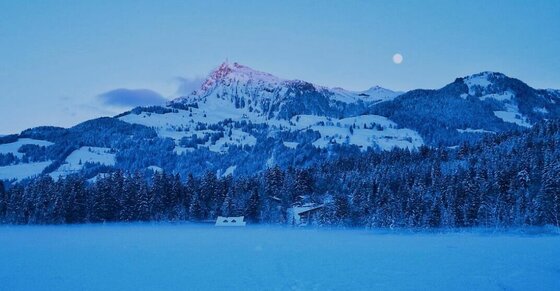 Schwarzsee im Winter Verschneite Berglandschaft mit Wald und Seeoberfläche in der Dämmerung unter Vollmond.