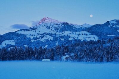 Schwarzsee im Winter Verschneite Berglandschaft mit Wald und Seeoberfläche in der Dämmerung unter Vollmond.
