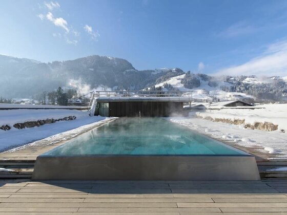 Dachpool im Winter Dampfender Außenpool auf einer Dachterrasse in einer verschneiten Gebirgslandschaft unter blauem Himmel.