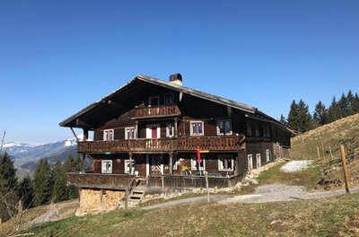 Zweistöckiges Holzhaus mit Balkonen am Hang vor blauem Himmel.